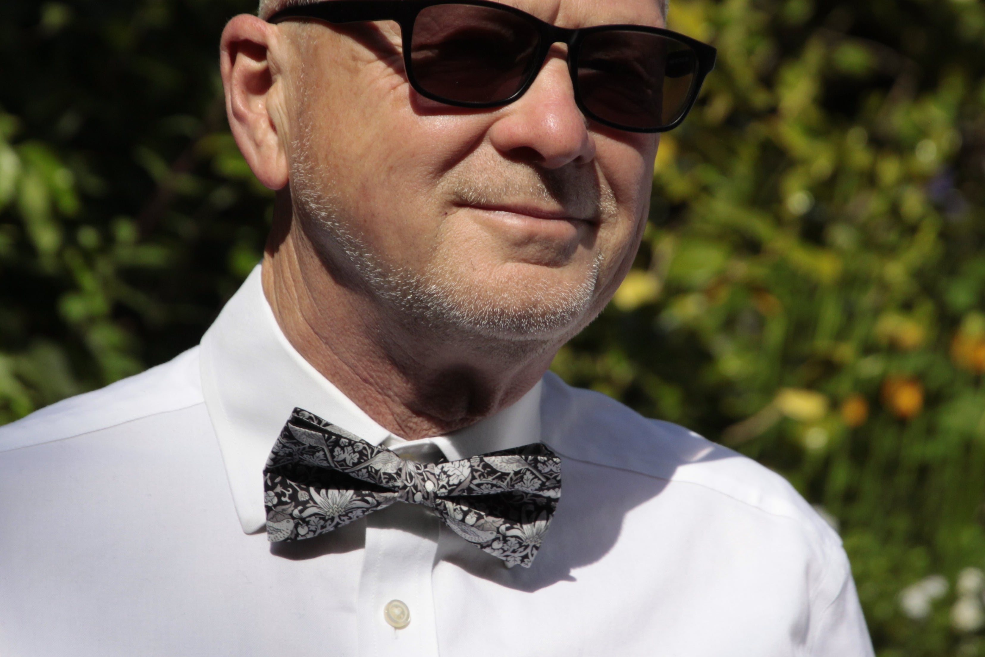 Man wearing sunglasses and a white shirt with a bow tie outdoors